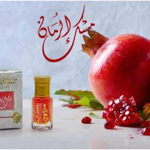 Gold-capped pomegranate perfume oil bottle labeled Musk Al Rumman sitting on snow with red fruit pieces – Arabic attar for men and women