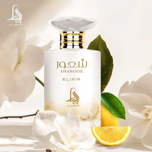 A bottle of Al Absar Shahoor elixir perfume with top notes listed as lemon, candy, and rum, middle notes as orange blossom and milk, and base notes as vanilla, benzoin, amber, and musk, presented alongside slices of lemon and a bar of soap.